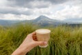 Woman`s hand holding a cup of coffee with a view of volcano Batur.