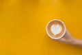 Woman`s hand holding a cup of Piccolo Latte art in small glass on yellow wooden desk
