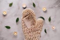 Woman's hand holding diy oats soap. Knitted sisal washcloth in mitten shape. Burning candles and marble background