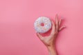 Woman`s hand holding a donut with colorful sprinkles on pink background Royalty Free Stock Photo