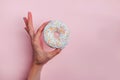 Woman`s hand holding a donut with colorful sprinkles on pink background Royalty Free Stock Photo