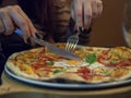 Woman`s hand holding fork and knife and cutting a delicious thin crust pizza. Royalty Free Stock Photo