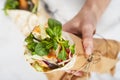 Woman`s hand holding a fresh tortilla wrap tied round with brown paper and string.