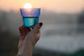 Woman`s hand holding glass against setting sun with blurry skyscrapers in cityscape background Royalty Free Stock Photo