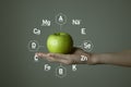 Woman`s hand holding green apple, microelement icons in molecular hexagons on grey background.