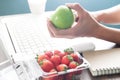 Woman`s hand holding green apple with strawberries in box on wor
