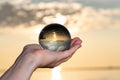 Woman`s hand holding high grade Clear Quartz Sphere at the sunrise in front of the lake