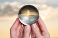 Woman`s hand holding high grade Clear Quartz Sphere at the sunrise in front of the lake