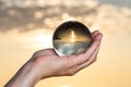 Woman`s hand holding high grade Clear Quartz Sphere at the sunrise in front of the lake