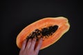 woman's hand holding juicy papaya halves on black background, tropical fruit close-up