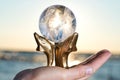 Woman`s hand holding Lemurian Clear Quartz Sphere on Dolphins Brass Stand at the sunrise Royalty Free Stock Photo