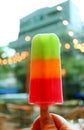 Woman`s hand holding a mix fruit ice bar against blurry building with bokeh lights Royalty Free Stock Photo