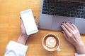 Top view mockup image of a woman`s hand holding mobile phone with blank white desktop screen while using laptop with coffee cup Royalty Free Stock Photo