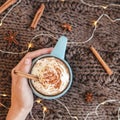 Woman`s hand holding mug of coffee, cocoa or hot chocolate with whipped cream and cinnamon on scarf with pumpkin, leaves Royalty Free Stock Photo