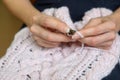 Woman`s hand holding needles and knitting pink clothing detail