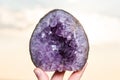 Woman`s hand holding partially polished Heart shaped Amethyst geode specimen from Brazil at sunrise in front of the lake