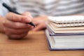 A woman`s hand holding a pen to write on a notebook and books on wooden table Royalty Free Stock Photo