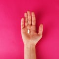 Woman`s hand holding a pill on the pink background Royalty Free Stock Photo