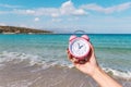 Woman`s hand is holding pink alarm clock on the beach background. Royalty Free Stock Photo