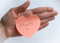 Woman`s hand holding pink heart-shaped sticky note with hand written word `Mum` on it on white background. Concept of love, minima Royalty Free Stock Photo