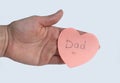 Woman`s hand holding pink heart-shaped sticky note with hand written word `Dad` on it on white background. Concept of love, minima Royalty Free Stock Photo