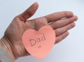 Woman`s hand holding pink heart-shaped sticky note with hand written word `Dad` on it on white background. Concept of love, minima Royalty Free Stock Photo