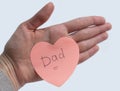 Woman`s hand holding pink heart-shaped sticky note with hand written word `Dad` on it on white background. Concept of love, minima Royalty Free Stock Photo