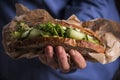 Woman`s hand holding a sandwich filled with fresh salad, cucumber and avocado.