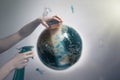 Woman`s hand holding a sponge and spray to clear the dirty planet Earth. The concept of improving the state of the environment,