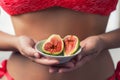Woman`s hand holding a two ripe sliced figs. Female in the bright bikini with fresh sweet exotic fruit