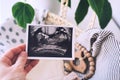 Woman`s hand holding ultrasound images in background of wicker basket of stuff for newborn baby Royalty Free Stock Photo