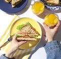 Woman`s hand is holding vegetarian wheat bran sandwich above the yellow plate. Healthy homemade breakfast concept flat lay.