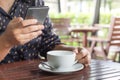 Woman`s hand holding a white coffee cup and smartphone in cafe blurred background  with morning sunlight Royalty Free Stock Photo