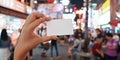 Woman`s hand holding a white empty card over crowded people at night street market as background. Royalty Free Stock Photo