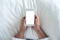 A woman`s hand holding white mobile phone with blank desktop screen on pillow and sitting in the bed Royalty Free Stock Photo