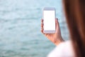A woman`s hand holding white mobile phone with blank desktop screen by the sea and blue sky background Royalty Free Stock Photo
