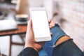 A woman`s hand holding white mobile phone with blank desktop screen on thigh in cafe Royalty Free Stock Photo