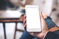 A woman`s hand holding white mobile phone with blank desktop screen on thigh in cafe Royalty Free Stock Photo