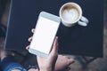 A woman`s hand holding white mobile phone with blank screen and hot coffee cup on a table in cafe Royalty Free Stock Photo