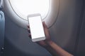 Woman`s hand holding a white smart phone with blank desktop screen next to an airplane Royalty Free Stock Photo