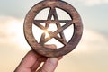 Woman`s hand holding Wooden encircled Pentagram symbol at sunrise in front of the lake. Concept of Five elements