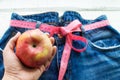 A woman`s hand holds an Apple against the top of a pair of denim trousers on a wooden background. Blue jeans with a measuring tap