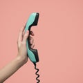 A woman`s hand holds blue retro telephone receiver. Pink background Royalty Free Stock Photo