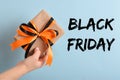 A woman& x27;s hand holds a gift box with a black-orange ribbon on a blue background. Black Friday. Royalty Free Stock Photo