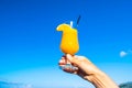 Woman\'s hand holds a glass of orange fresh juice with a straw and an orange slice against the background of a blue sky Royalty Free Stock Photo