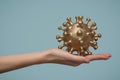 Woman`s hand holds a gold-colored virus model. Blue background