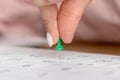 A female hand with a beautiful manicure holds a green pushpin to mark the date on the calendar Royalty Free Stock Photo