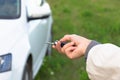 A woman`s hand holds the key to a new white car and opens it on a bright sunny summer day against a background of green grass Royalty Free Stock Photo