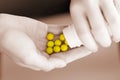 A woman`s hand holds a medicine and pours yellow pills into her hand from a bottle in close-up. Hands of a young girl holding a wh Royalty Free Stock Photo