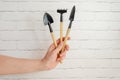 woman's hand holds miniature gardening tools against white brick wall. Tools for caring for plants